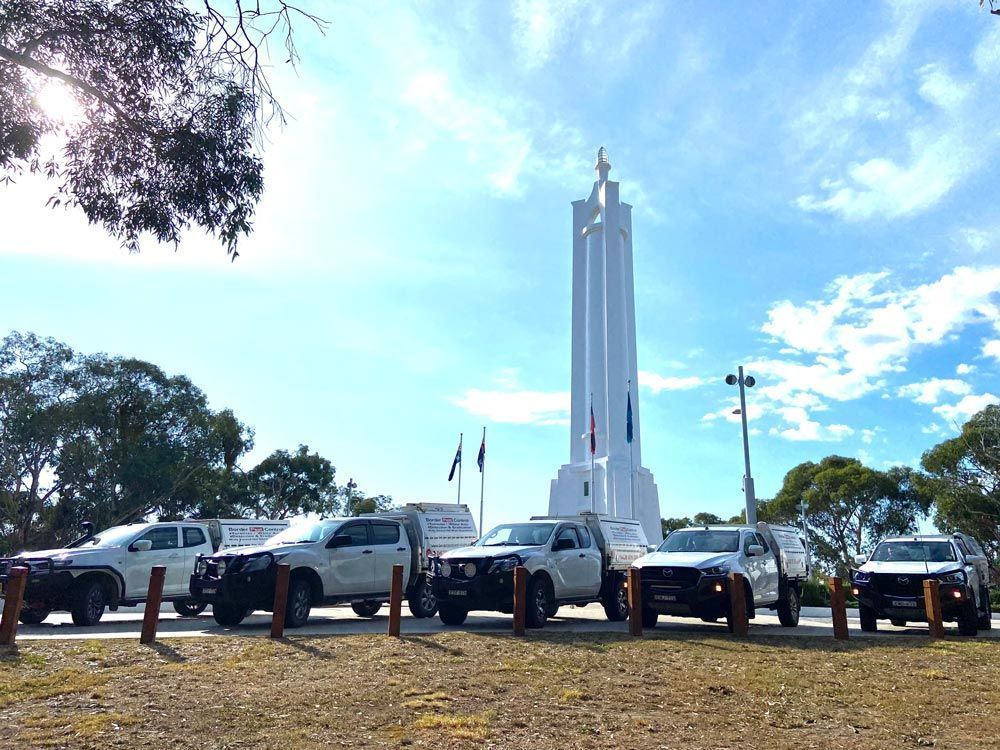 A Row of White Trucks Are Parked in Front of a Statue — Border Pest Control In Albury, NSW
