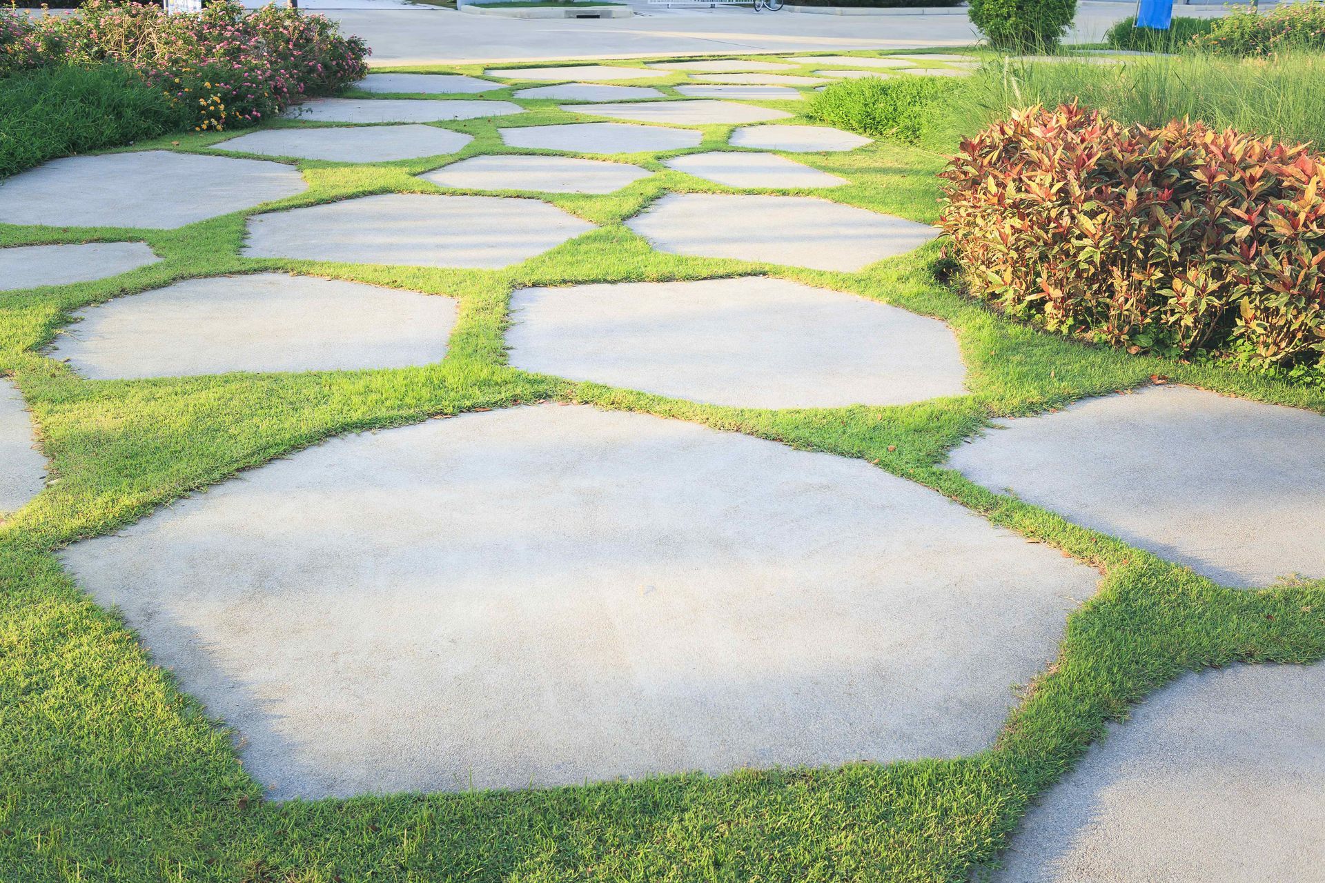 Large odd shaped pavers on grass with garden beds to each side.