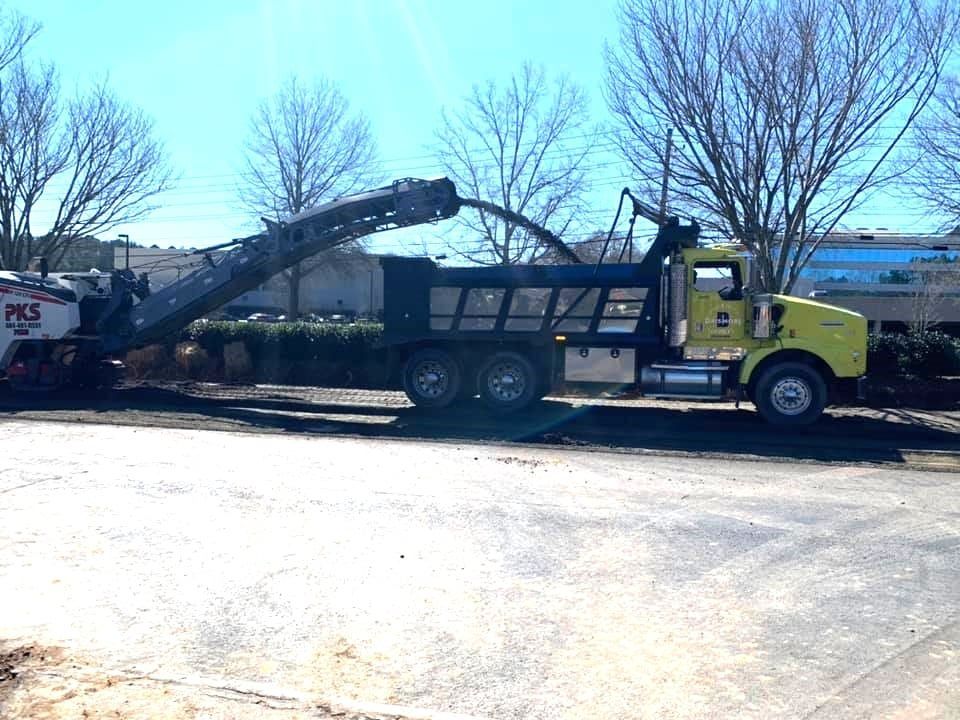Yellow truck loading asphalt debris from a milling machine on a sunny day.