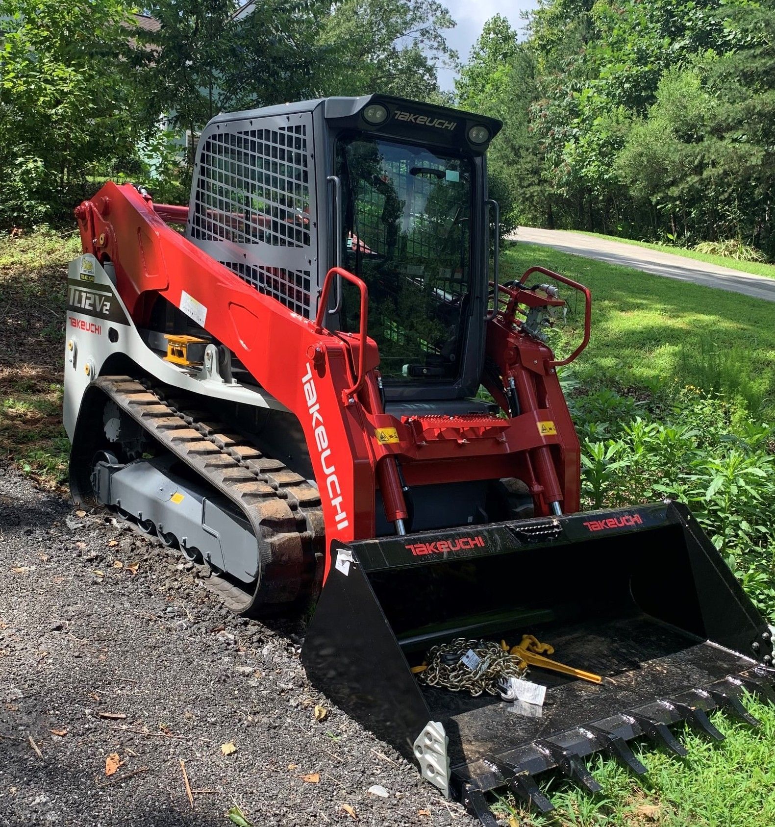 A white and red Takeuchi track skid steer loader on a gravel surface next to greenery.