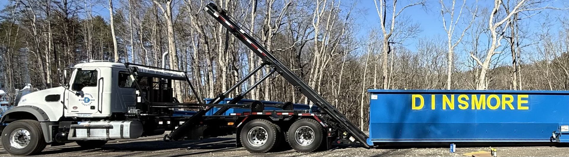 A white truck lifting a blue dumpster with 
