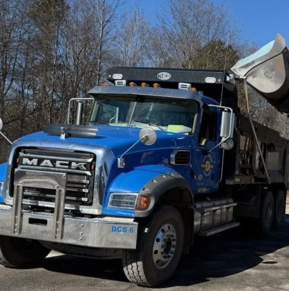 Blue Mack dump truck with its bed raised, parked outdoors.