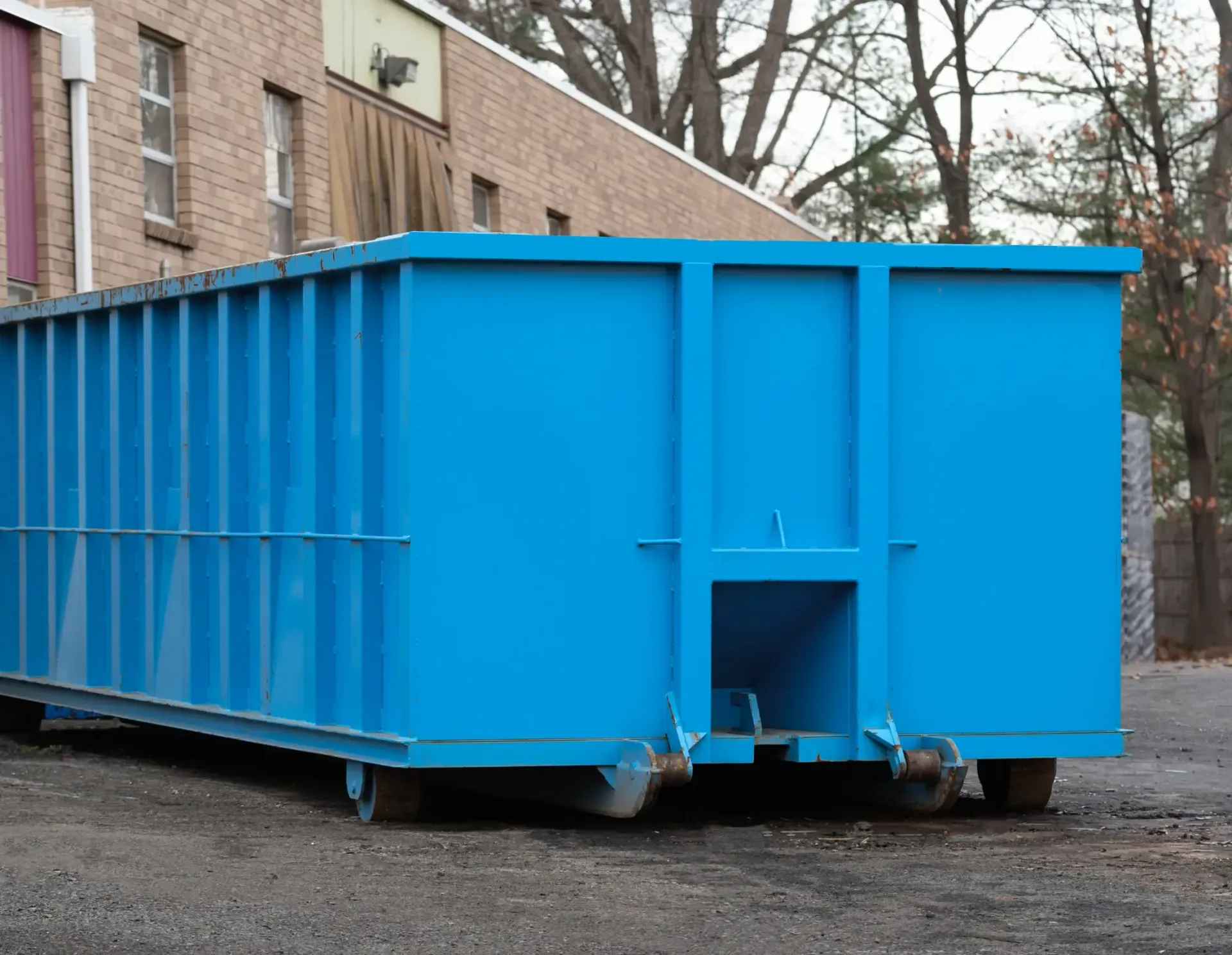 Brown Grogan Waste dumpster filled with debris, on grass in front of a brick building.
