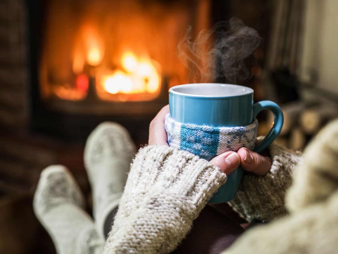 Warming and relaxing near a fireplace with a cup of hot drink.