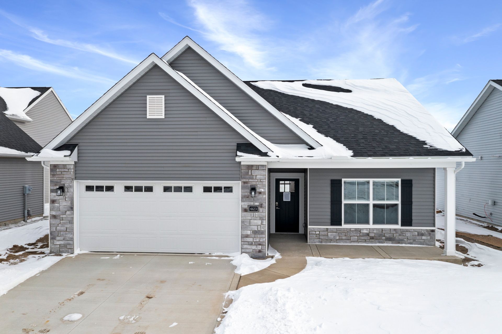Gray house with stone accents, snow on roof and ground, white garage door.