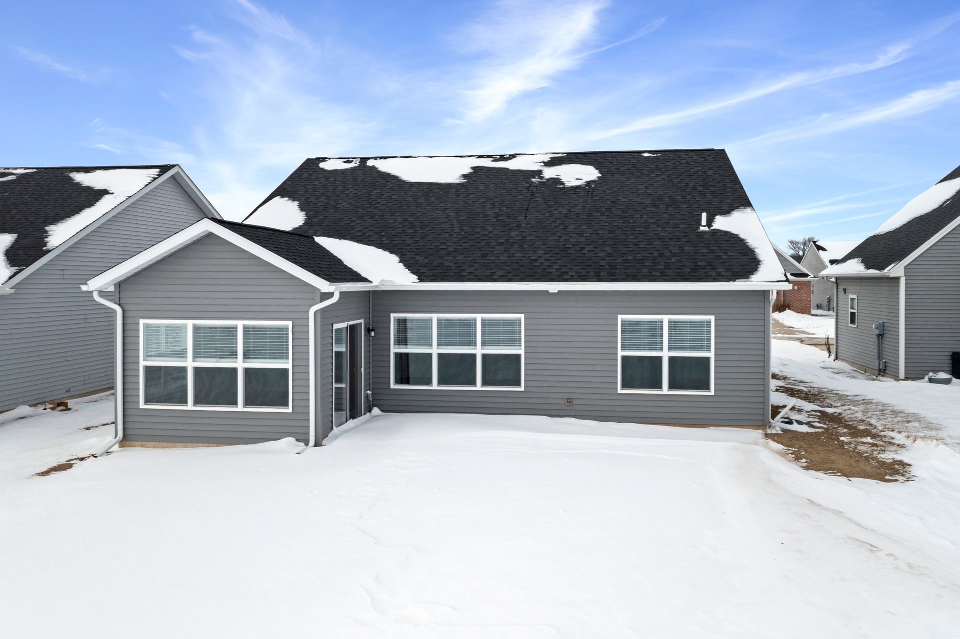 Gray house with snow-covered roof and yard; winter setting.