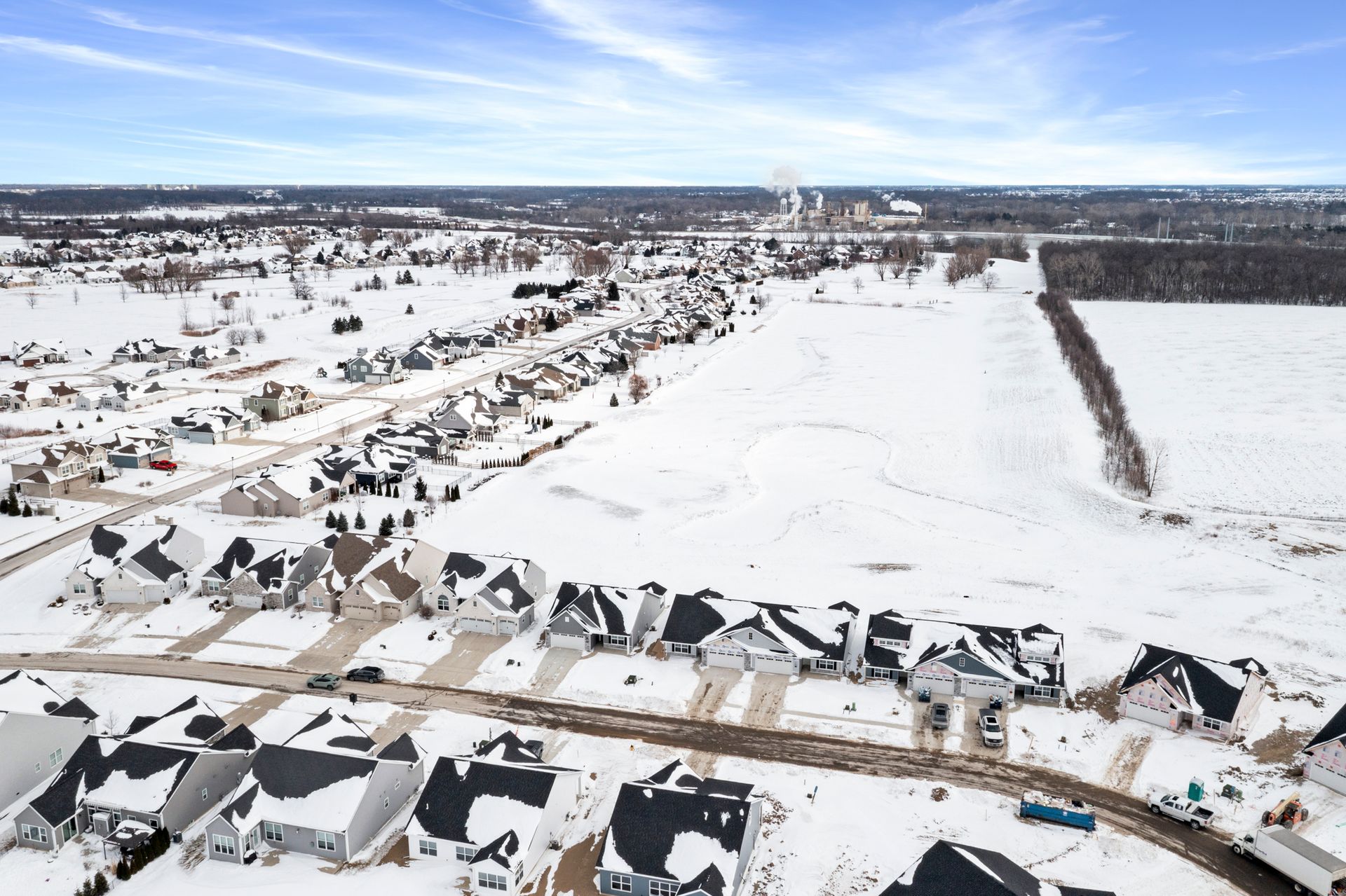 Snow-covered suburban neighborhood with houses, a snowy field, and a cloudy sky in winter.