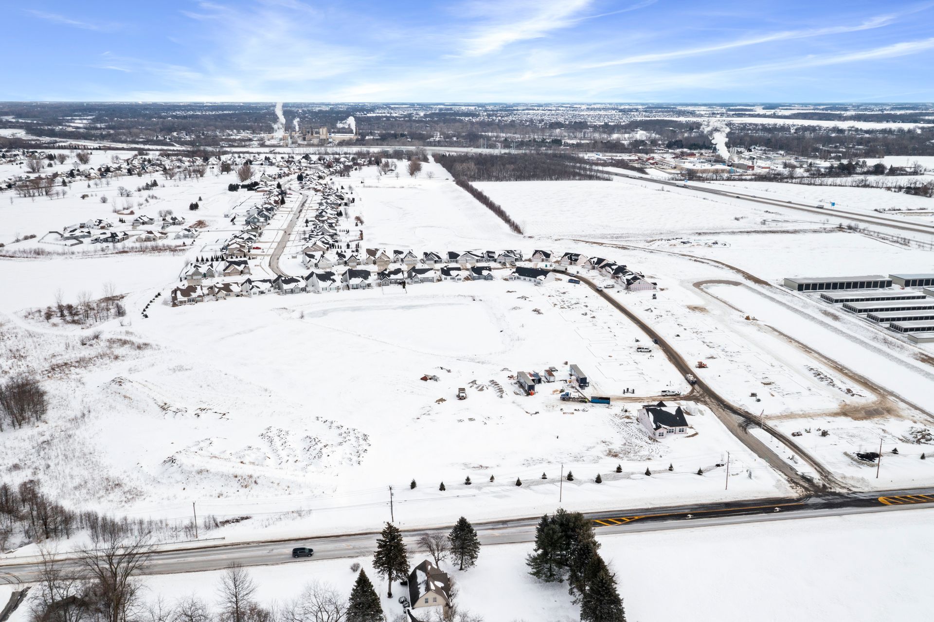 Aerial view of snowy rural landscape with buildings, roads, and a clear blue sky.