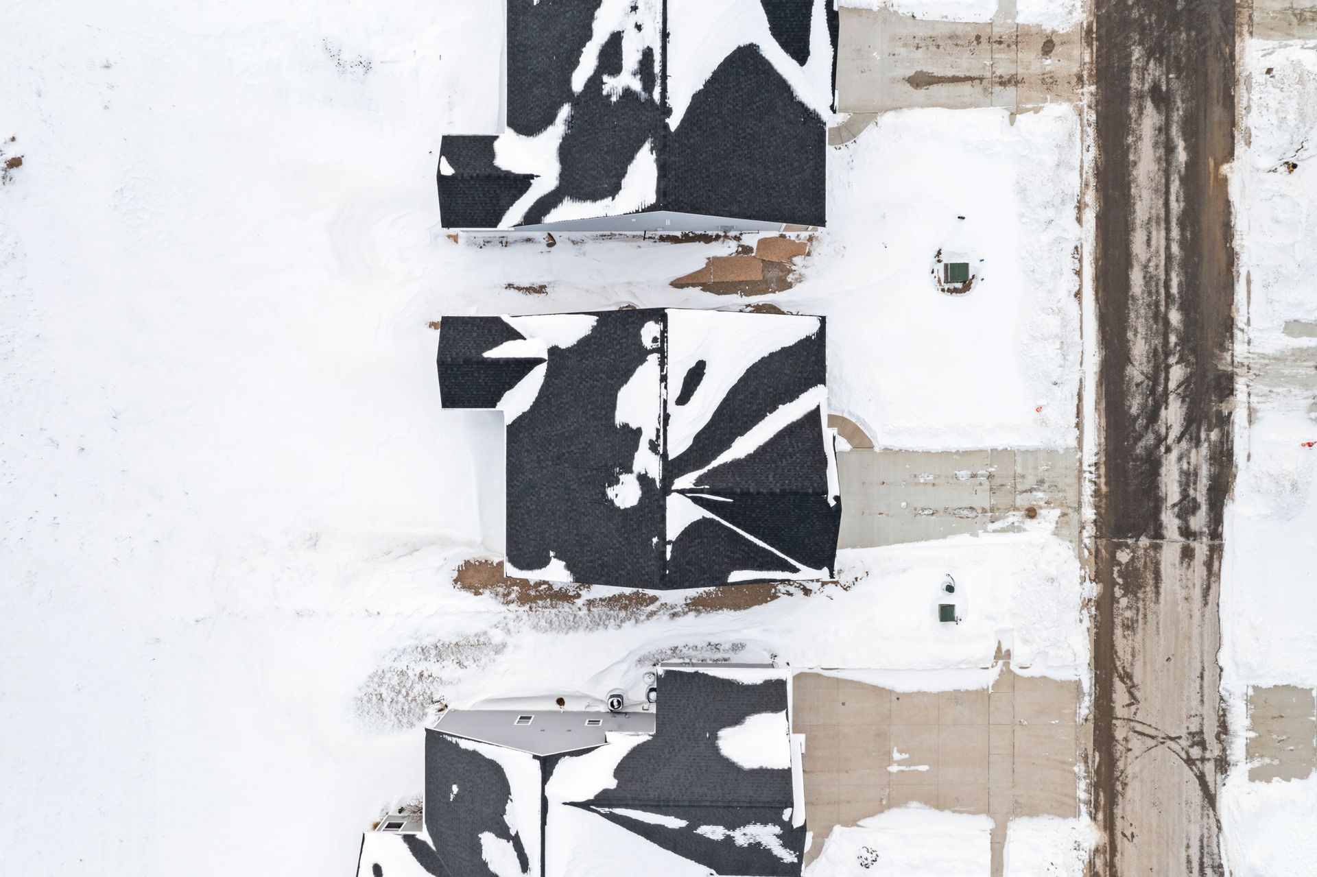 Overhead view of snow-covered rooftops in a residential area, with a street on the right.