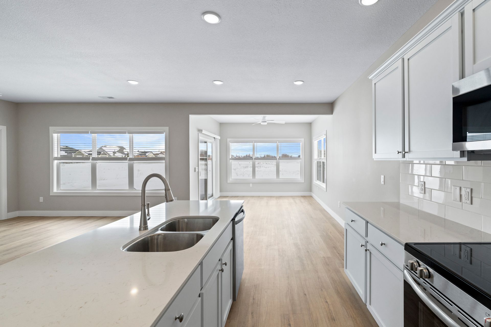 Modern kitchen with white cabinets, light wood floors, and island. Windows overlook outside.