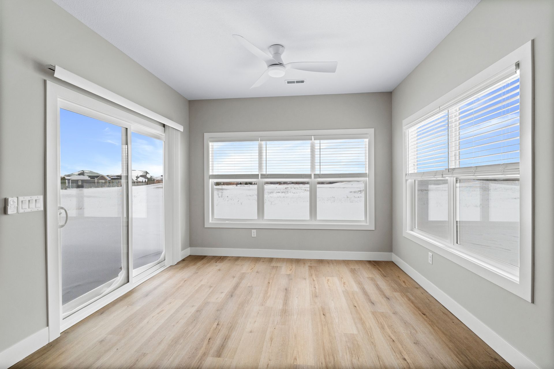 Empty room with light wood floors, gray walls, white-framed windows, and a sliding door.