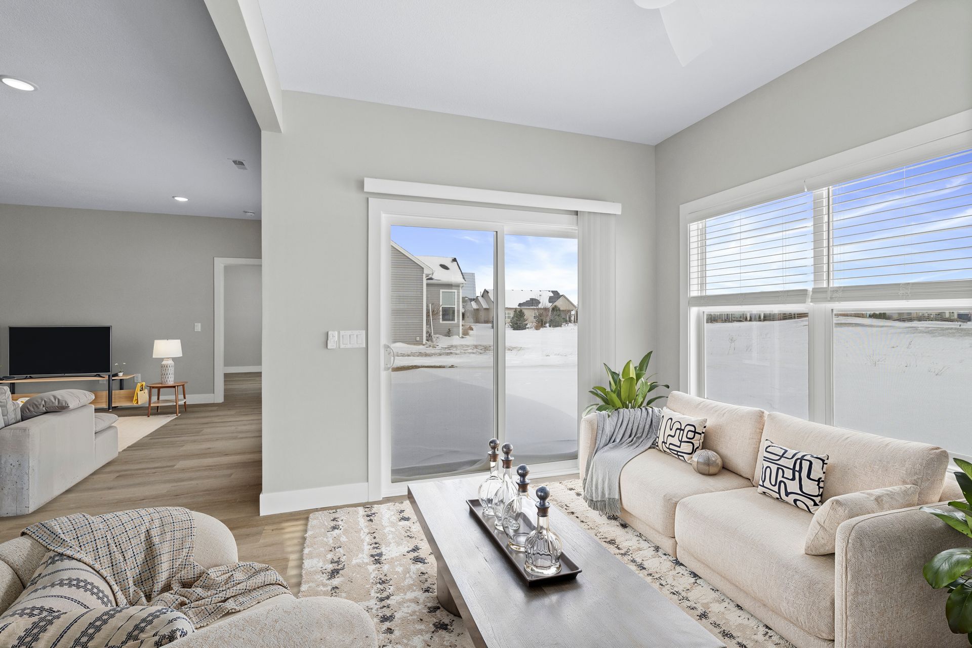 Bright living room with snowy outdoor view through sliding glass door and window. Beige couch, rug, and walls.