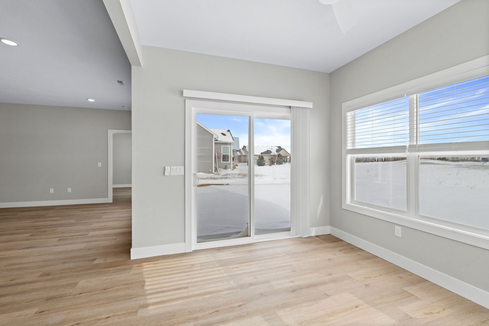 Light-filled room with sliding glass door and window overlooking snowy scene; pale wood floors.