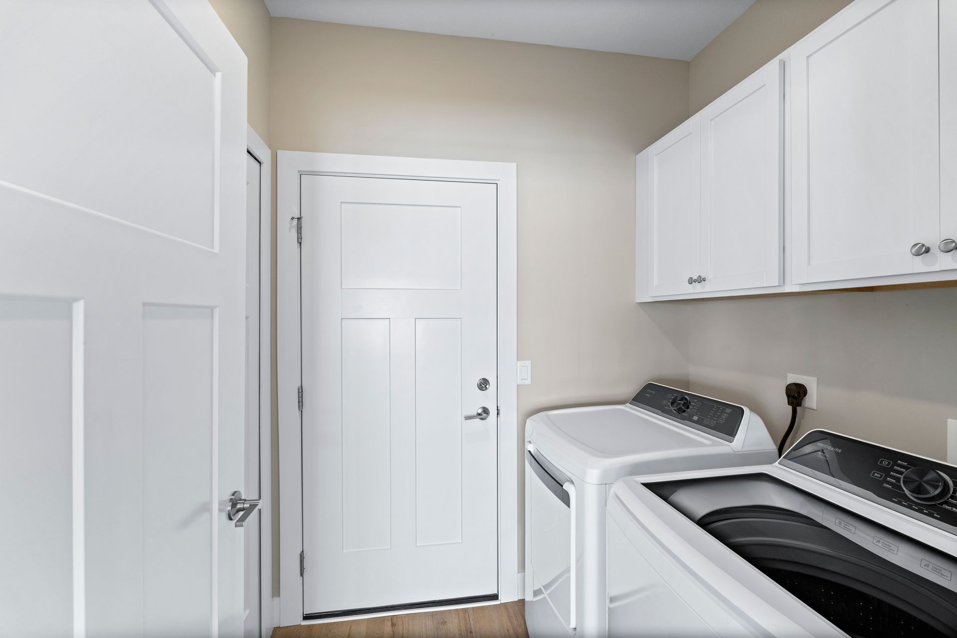 Laundry room with white washer and dryer, cabinets, and a door.