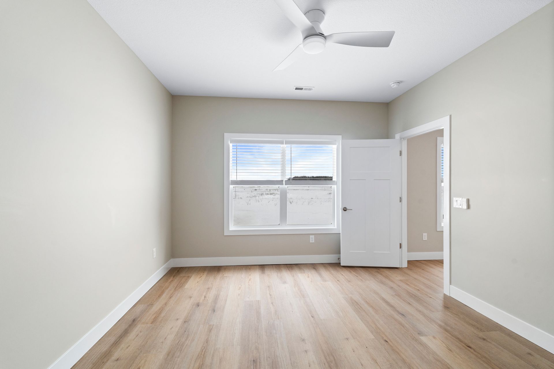 Empty room with light wood floors, a window, and a white ceiling fan.