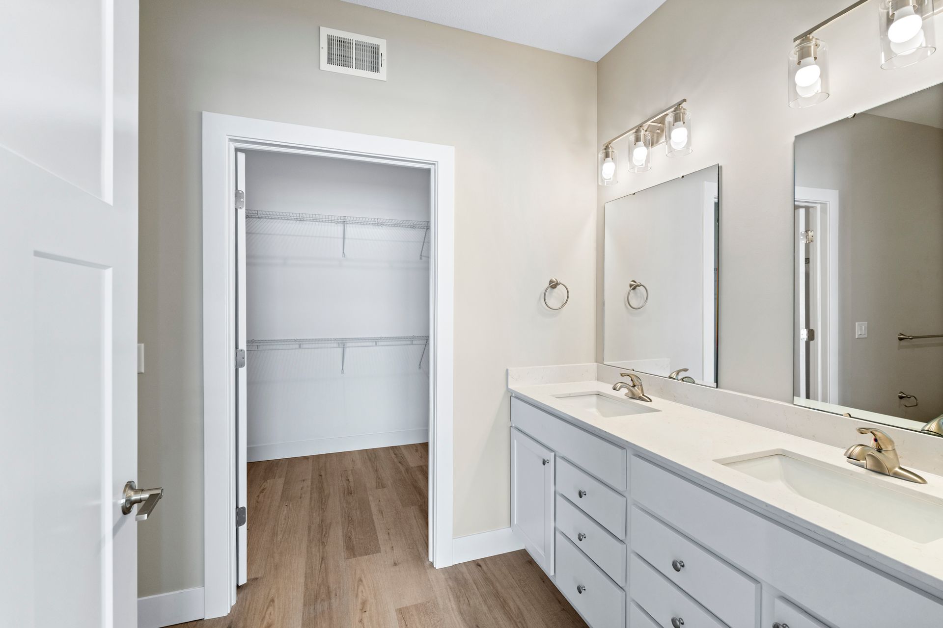 Bathroom with double sinks, white vanity, and walk-in closet with shelves.