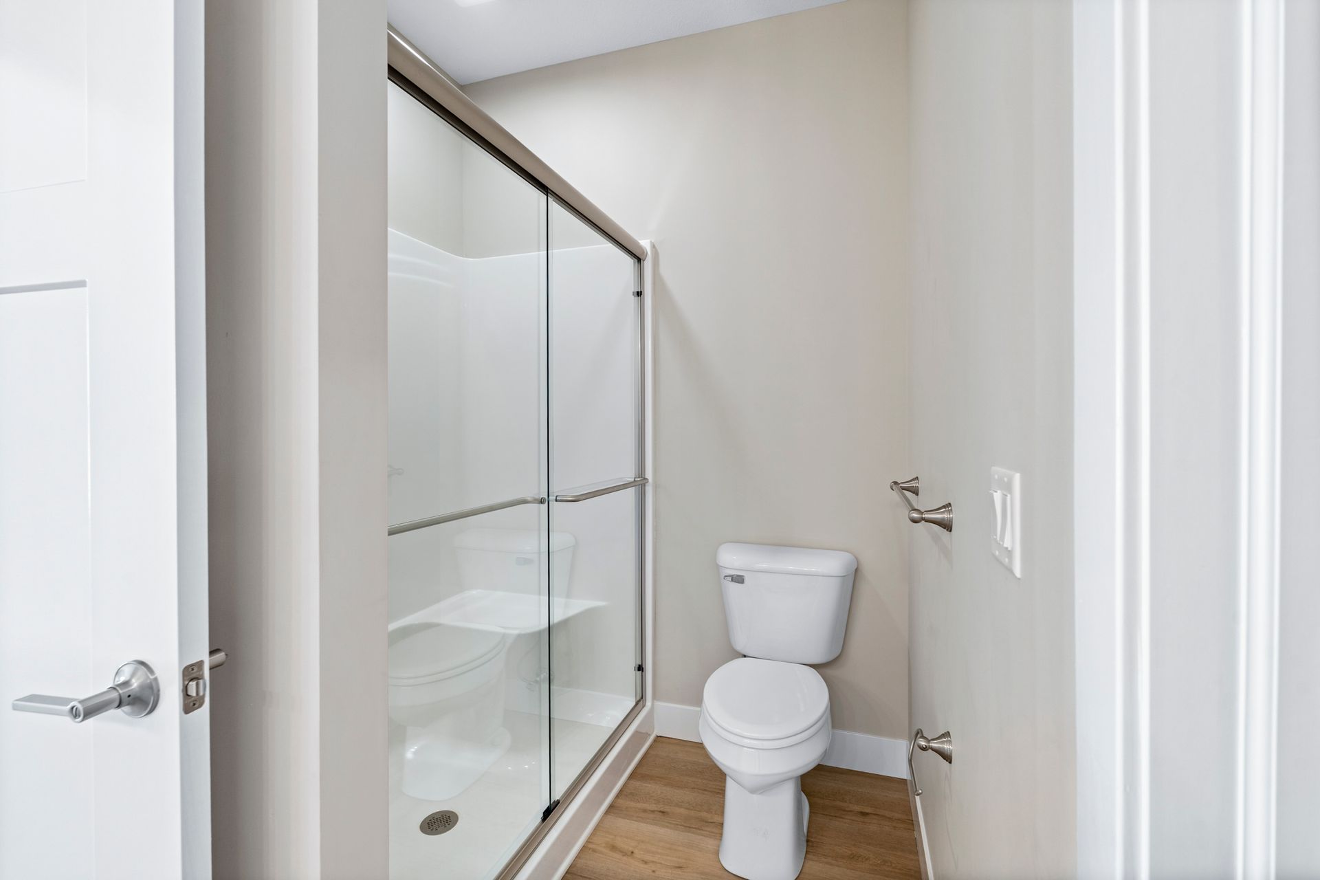 Small, neutral-toned bathroom with a shower, toilet, and towel rack.