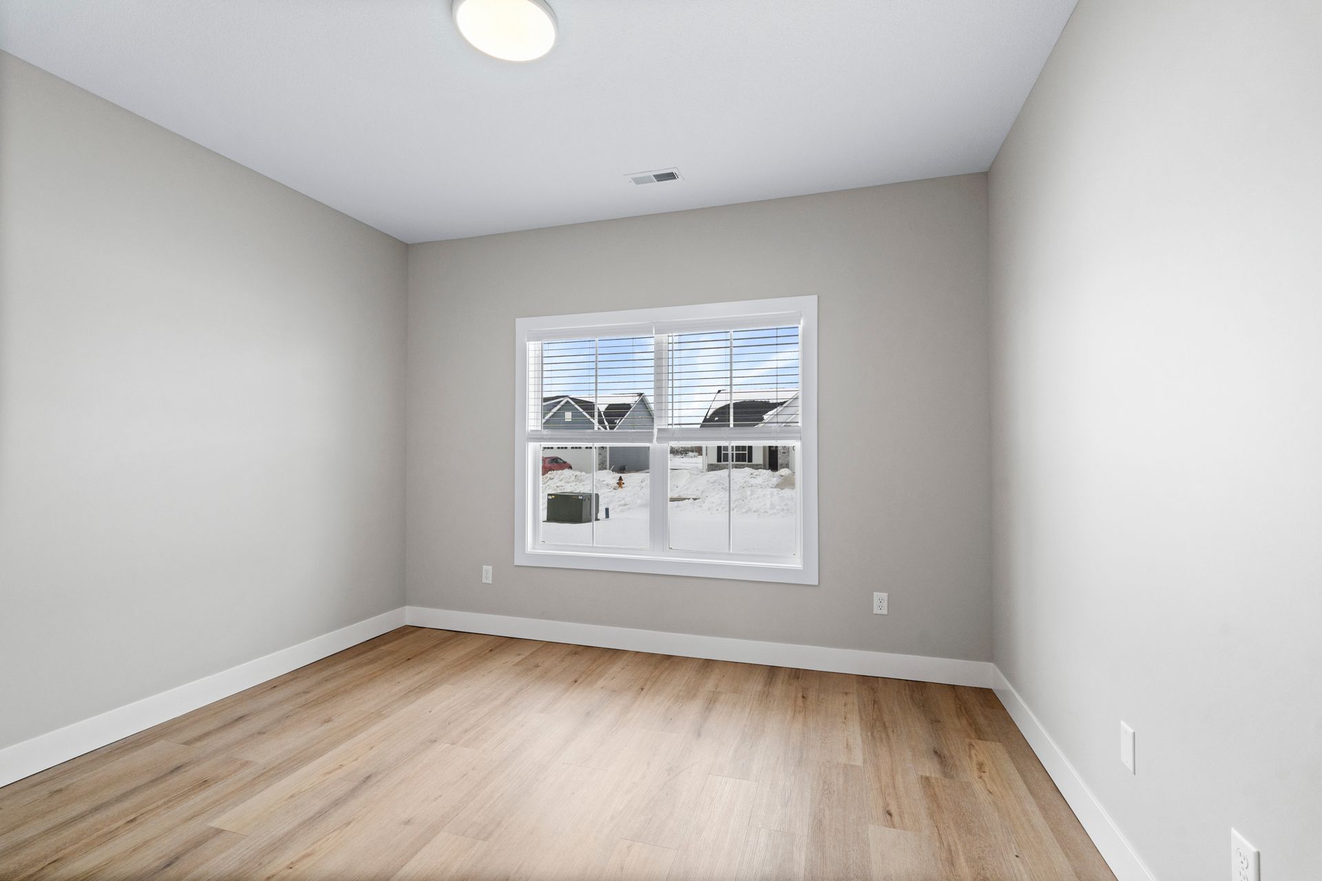 Empty room with light wood floors, a window, and gray walls.