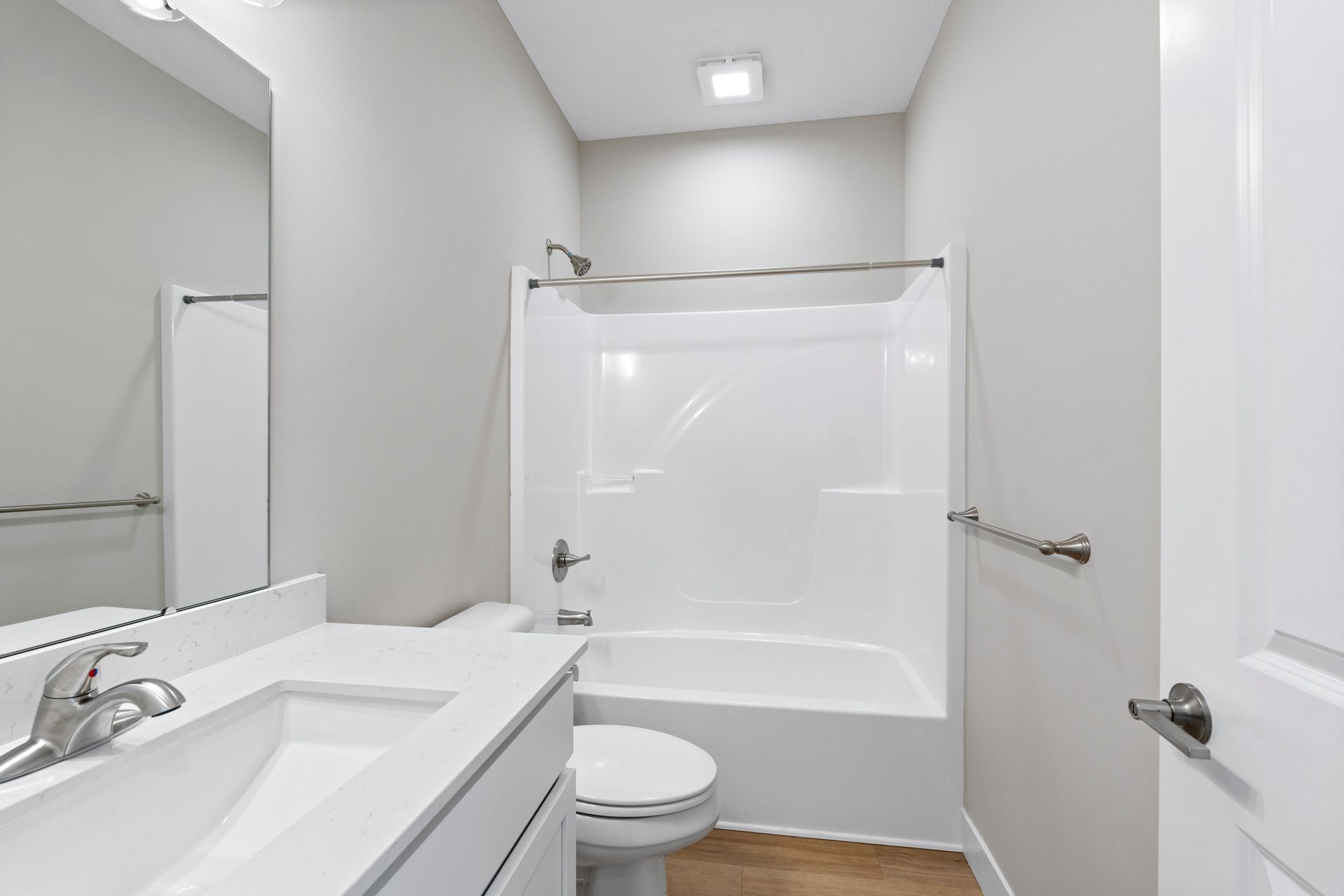 White bathroom with tub/shower, vanity with sink, toilet, and towel bar.