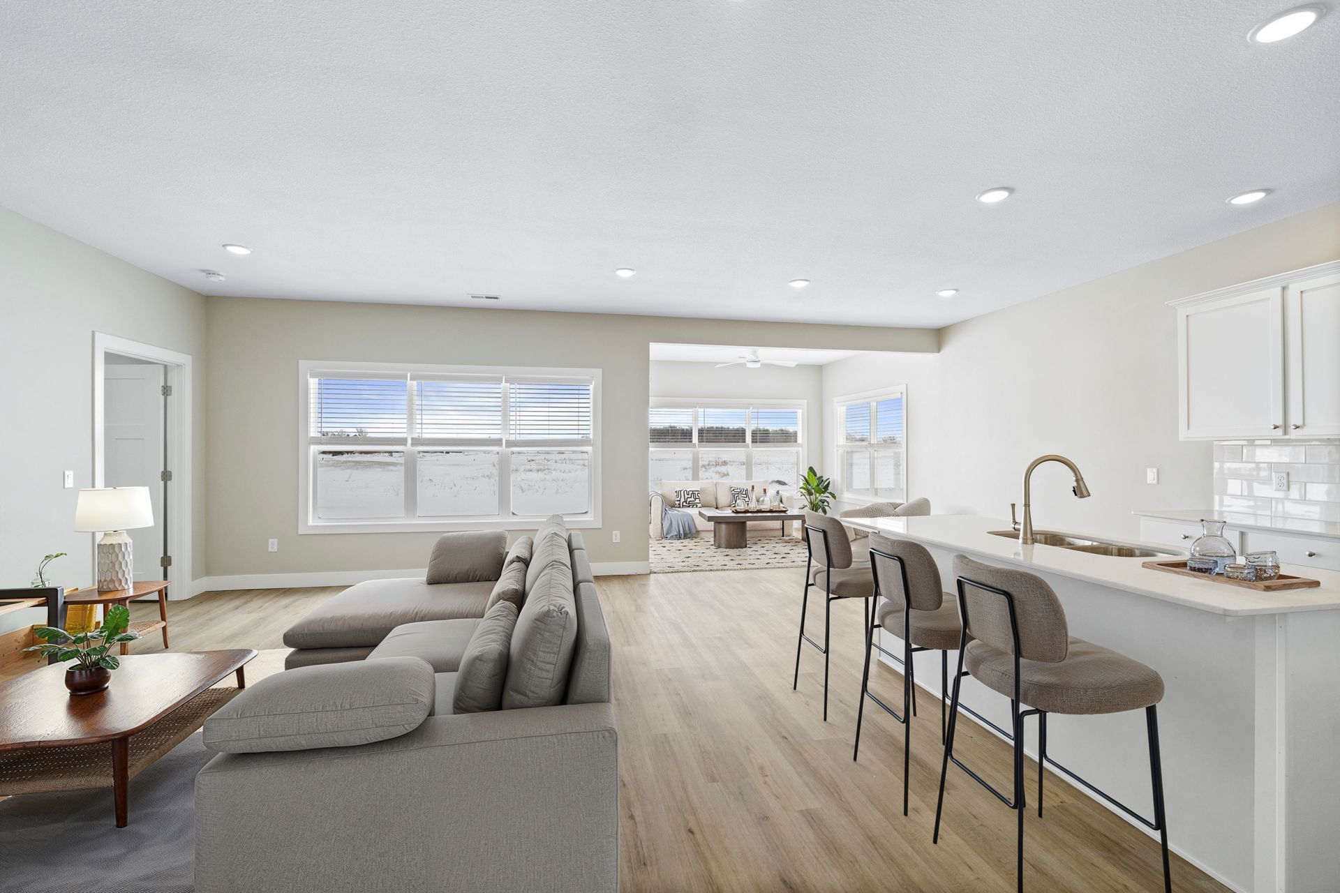 Open-concept living space with a kitchen and living room, gray sectional sofa, and kitchen island with bar stools.