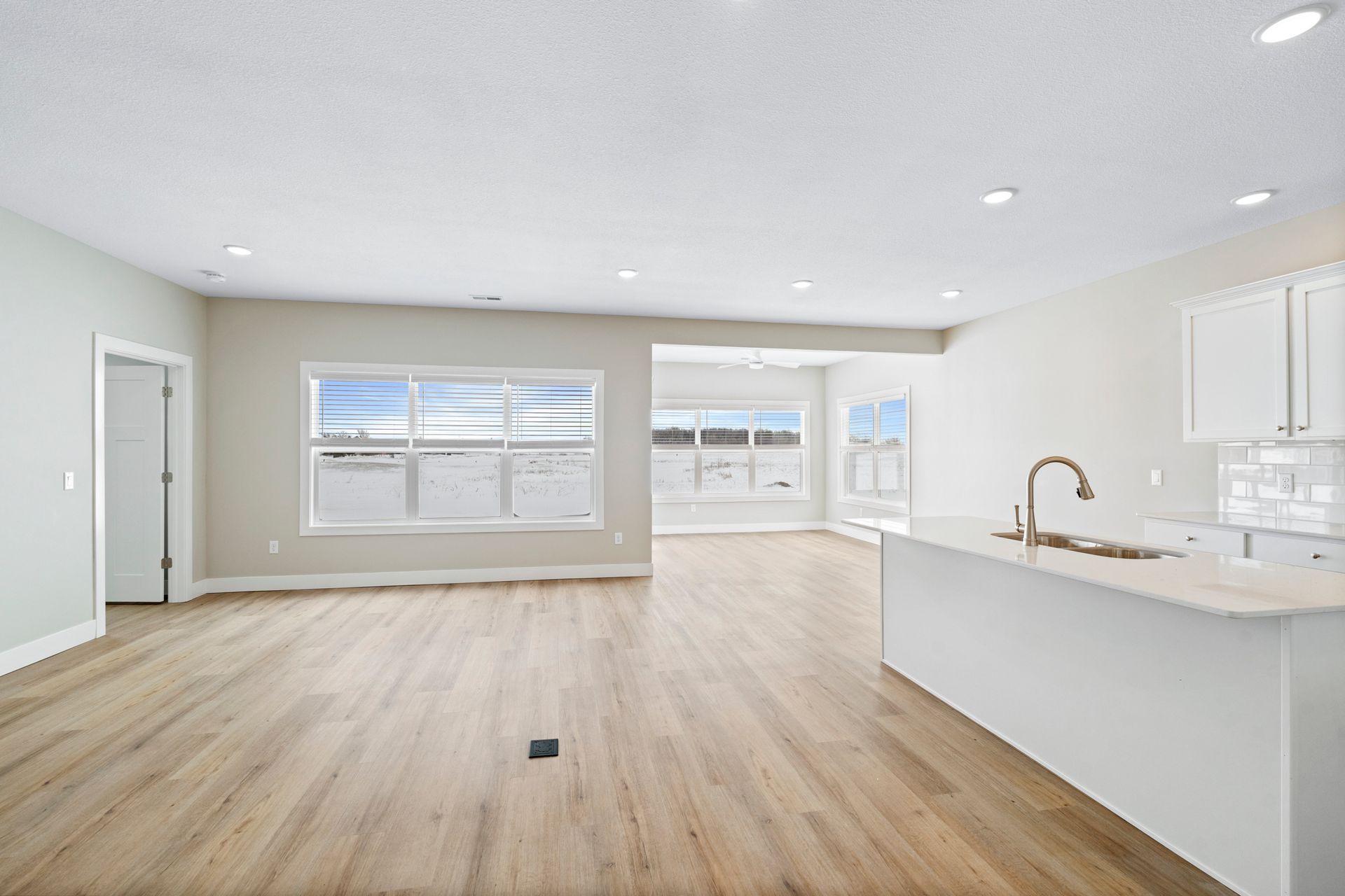 Empty, bright living area with wood floors, white cabinets, and large windows.