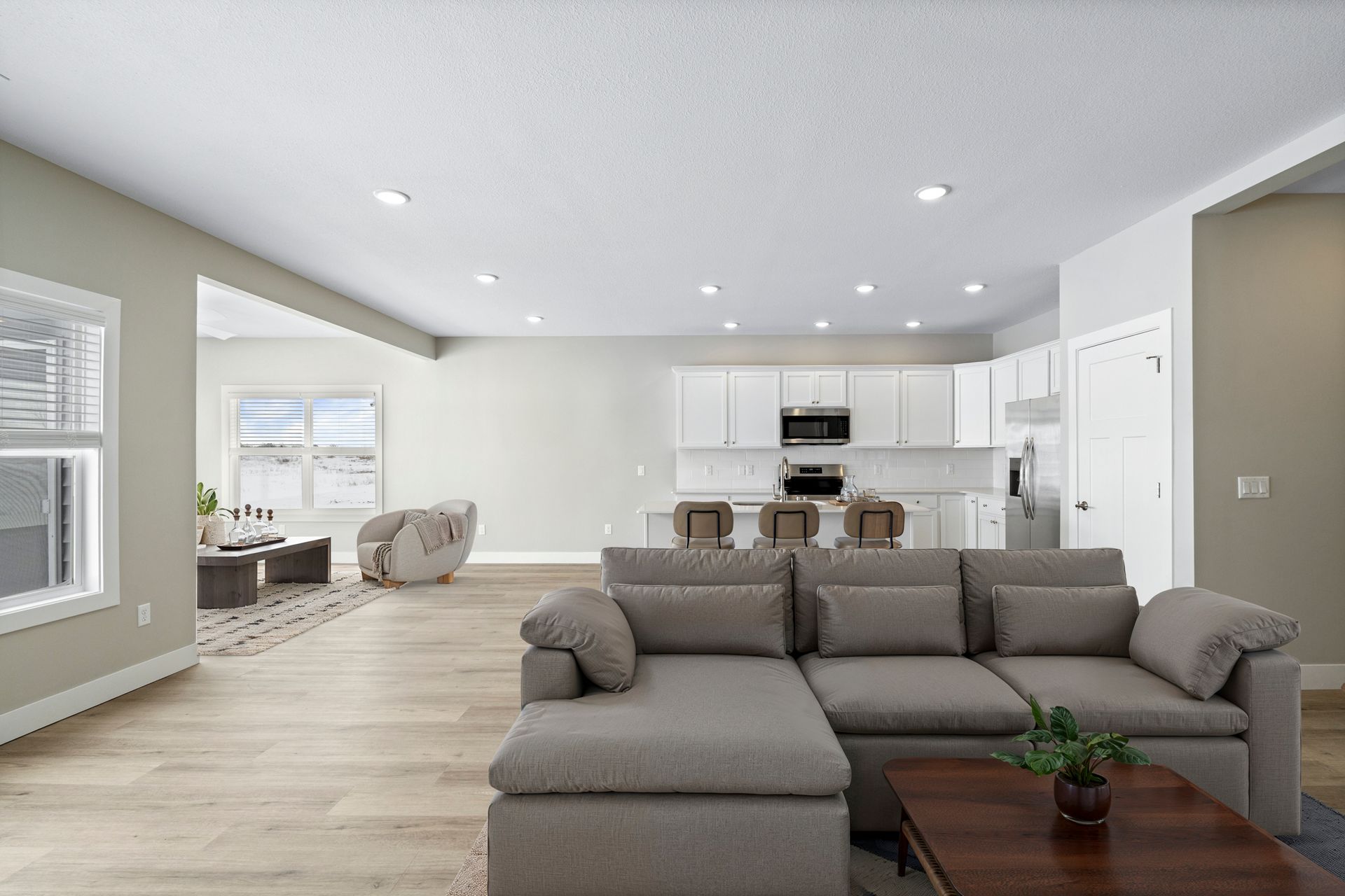 Open-concept living space with a gray sectional sofa, kitchen, and large windows.