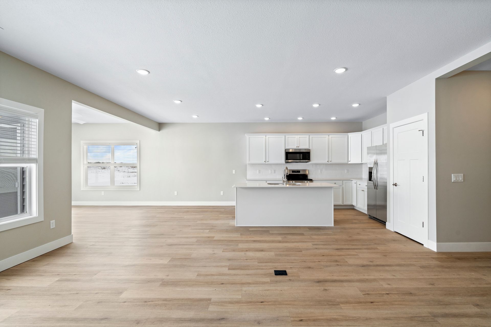 Open-concept interior with white kitchen, island, and light wood flooring.