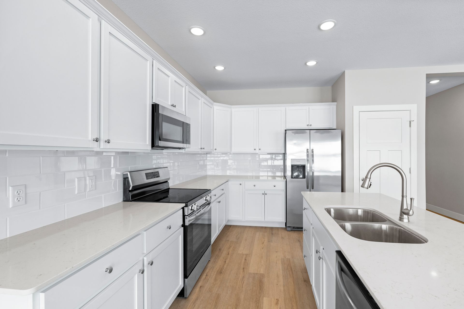 White modern kitchen with stainless steel appliances, light countertops, and wooden floors.
