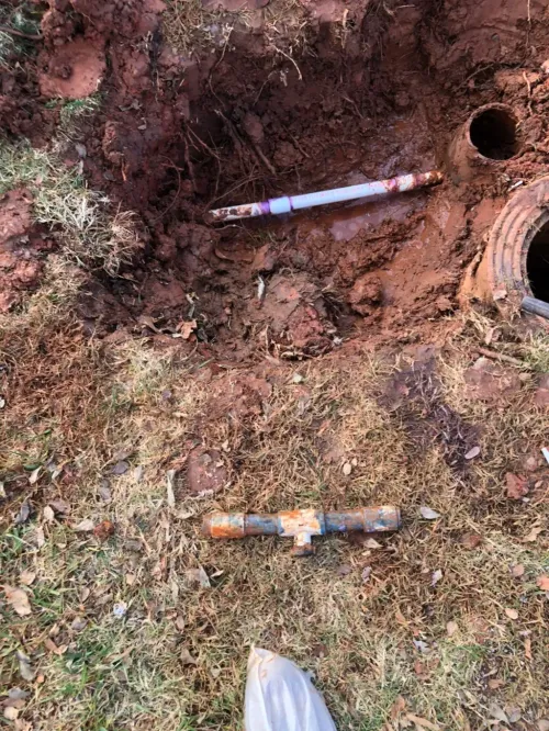 A hose is laying in the dirt next to a hole in the ground.