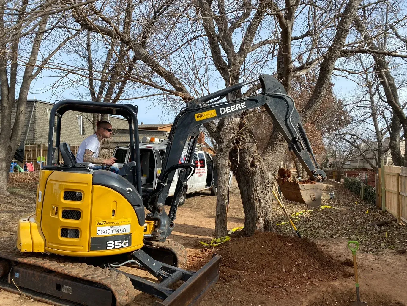 A man is driving a small excavator in a yard.