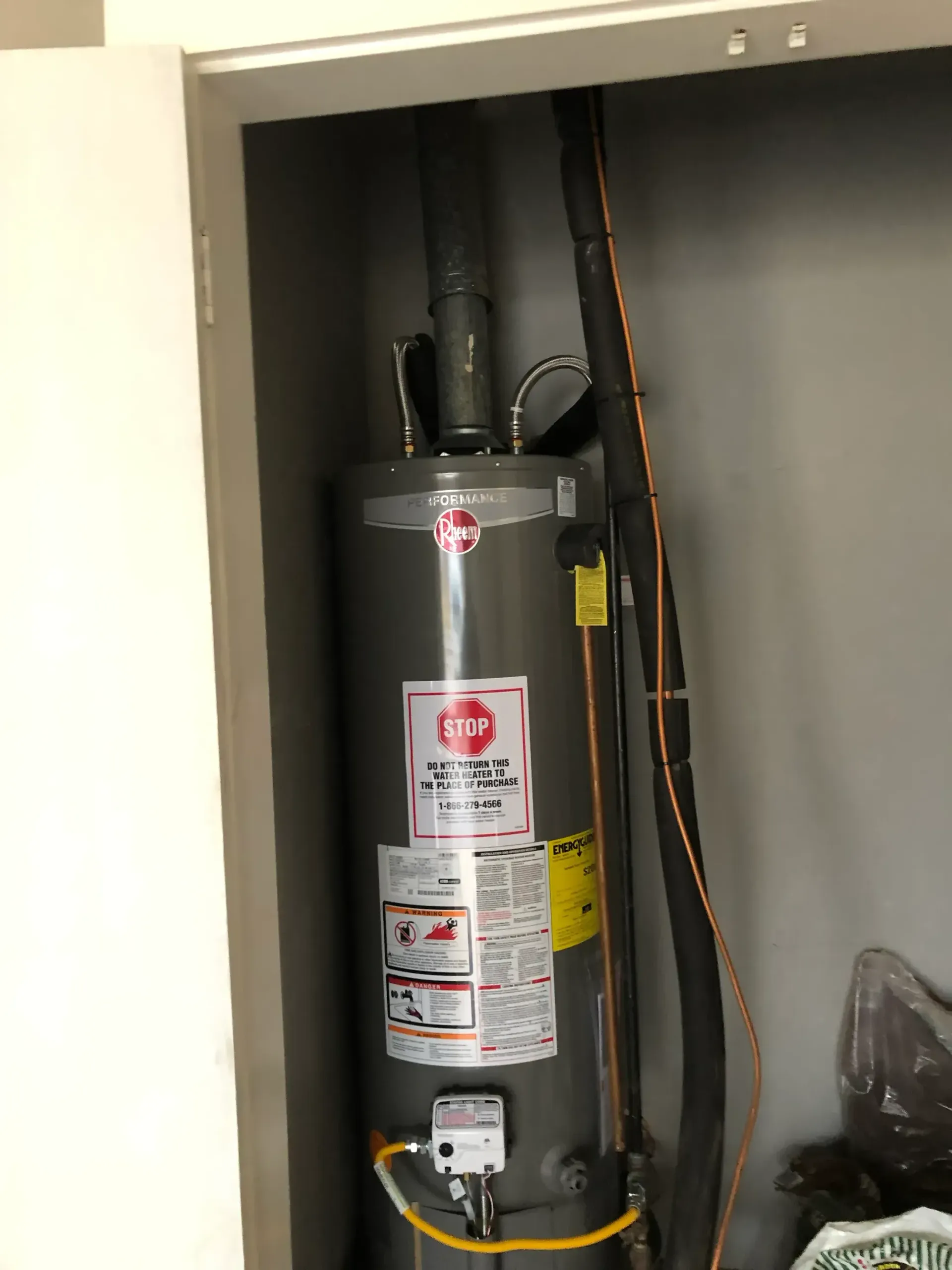 A water heater is sitting in a closet next to a wall.