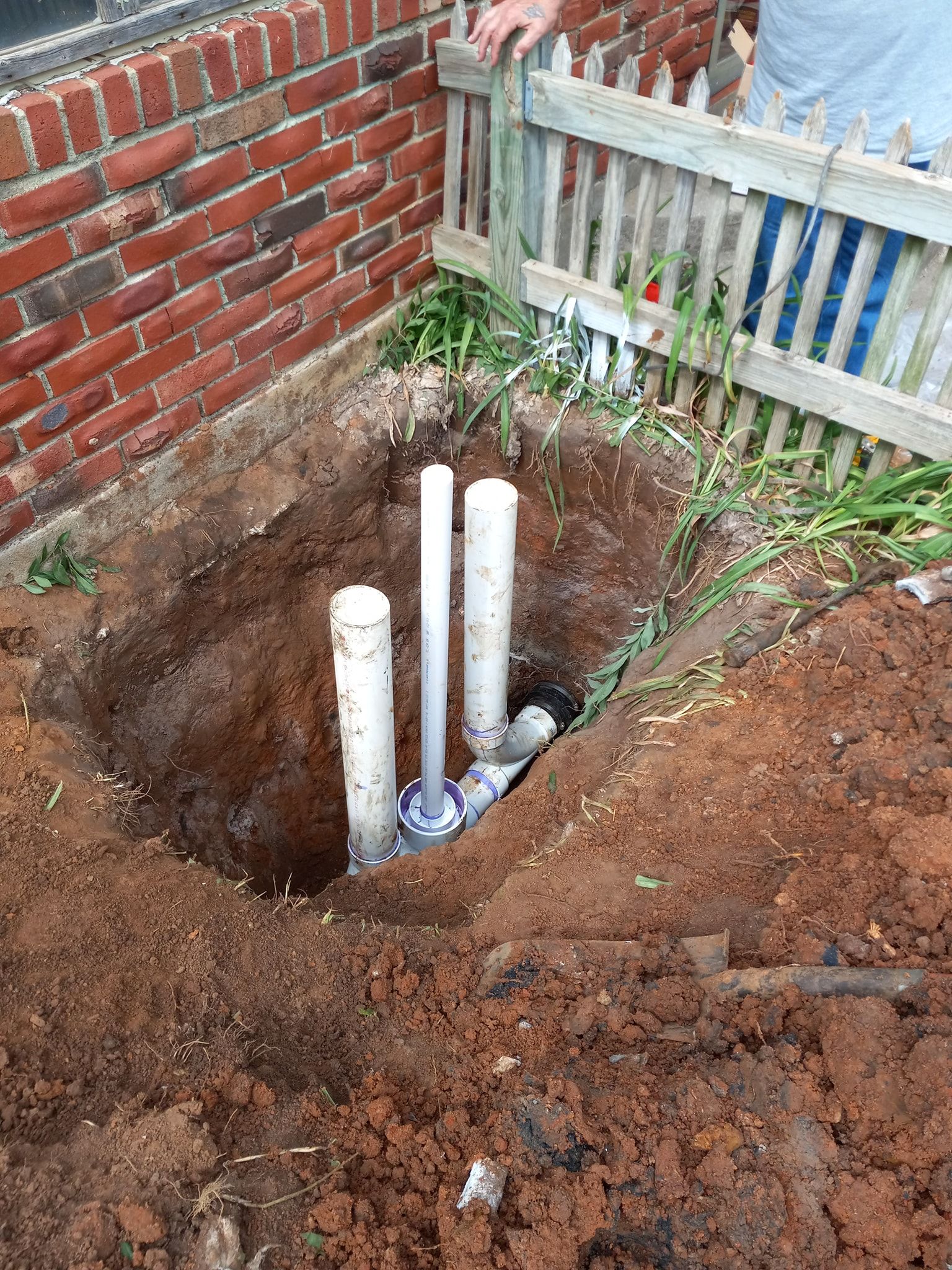A person is digging a hole in the ground next to a brick wall.