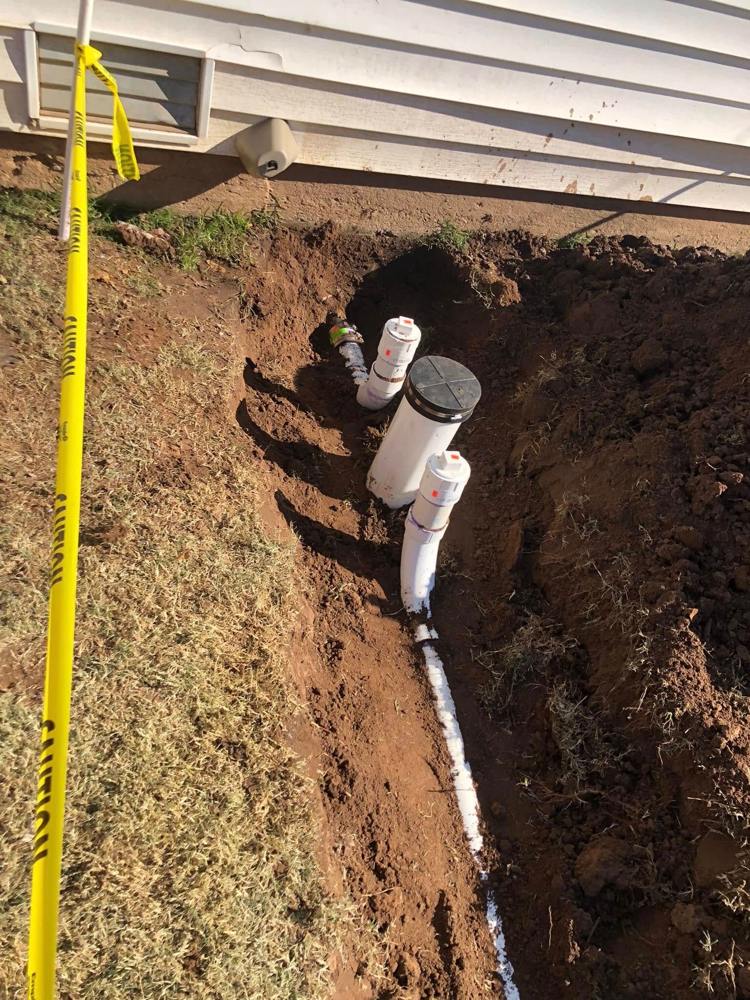 A drain pipe is being installed in the dirt next to a house.