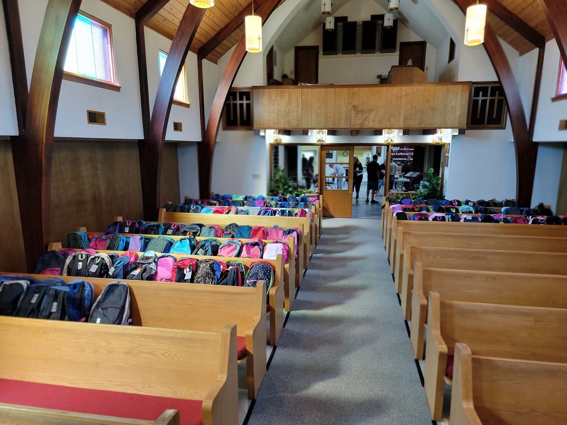Church interior with rows of pews filled with backpacks; doorway at the end.