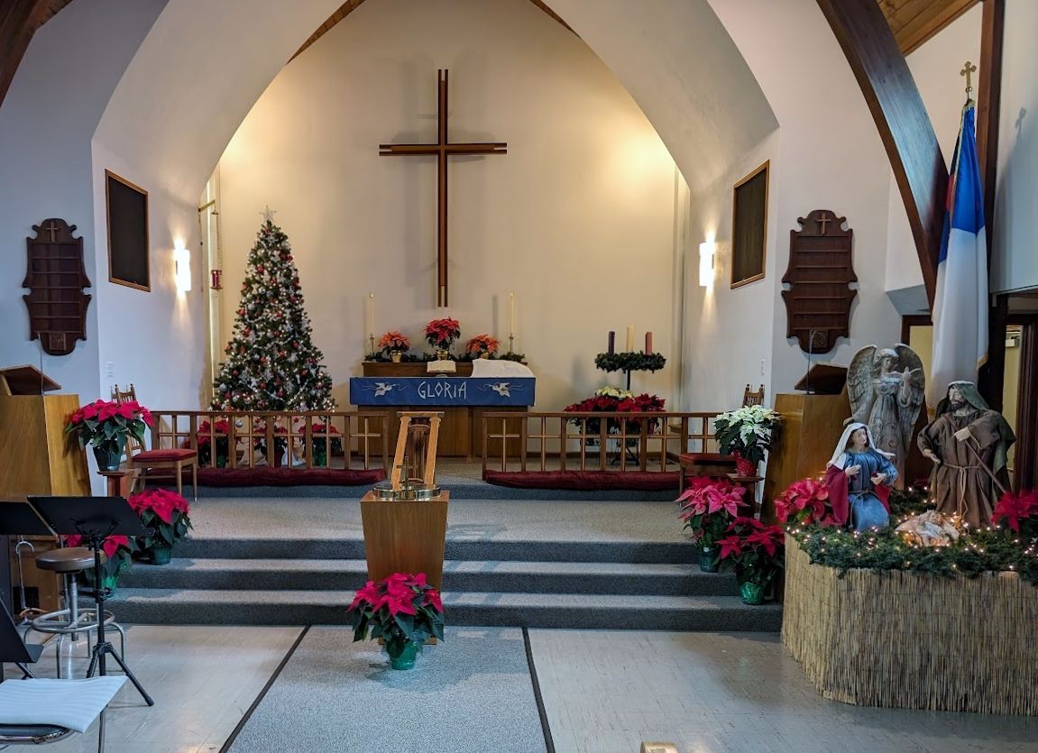 Interior of a church decorated for Christmas, with a cross, Christmas tree, and nativity scene.