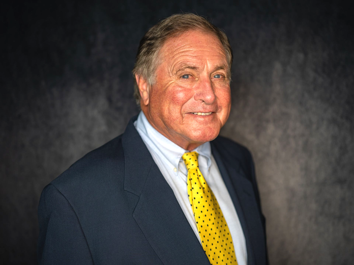 Man in blue suit and yellow polka dot tie, smiling at the camera against a dark backdrop.