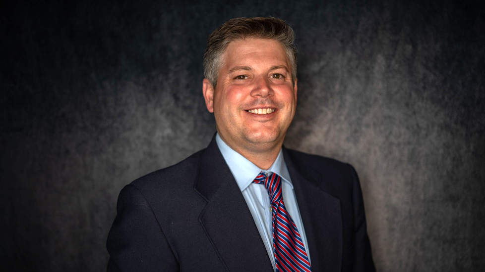 Man in suit smiles at the camera against a dark, textured background.