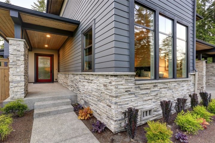 Modern house entrance with stone façade, gray siding, front steps, and landscaping