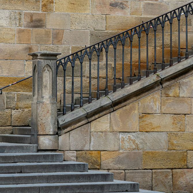 Stone staircase with black iron railing beside a tan brick wall