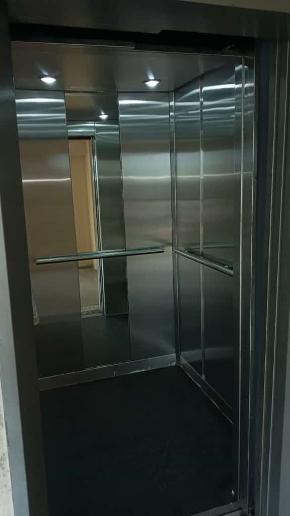 El interior de un ascensor de acero inoxidable con suelo negro.