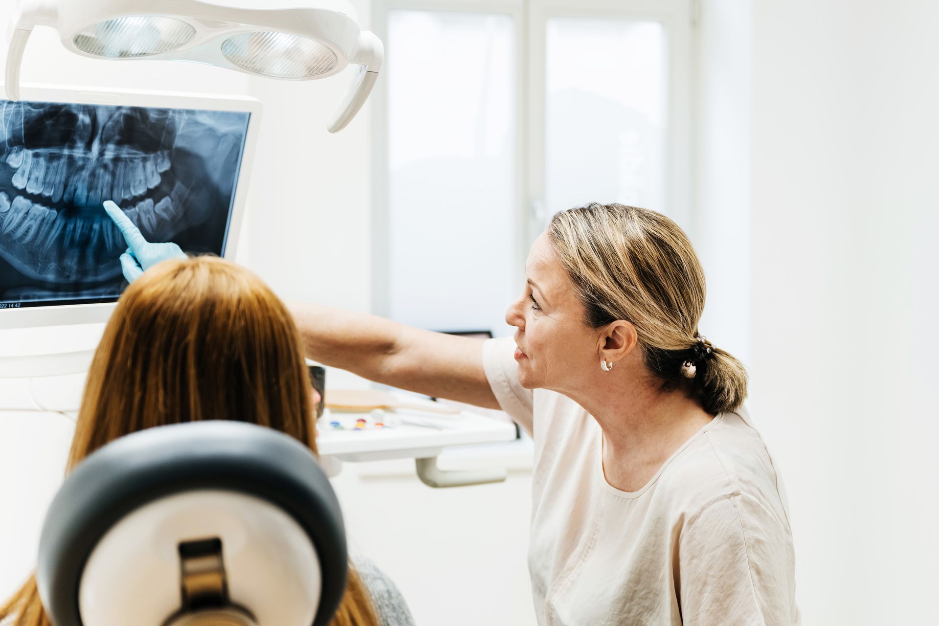 A woman is sitting in a dental chair looking at an x-ray of her teeth.