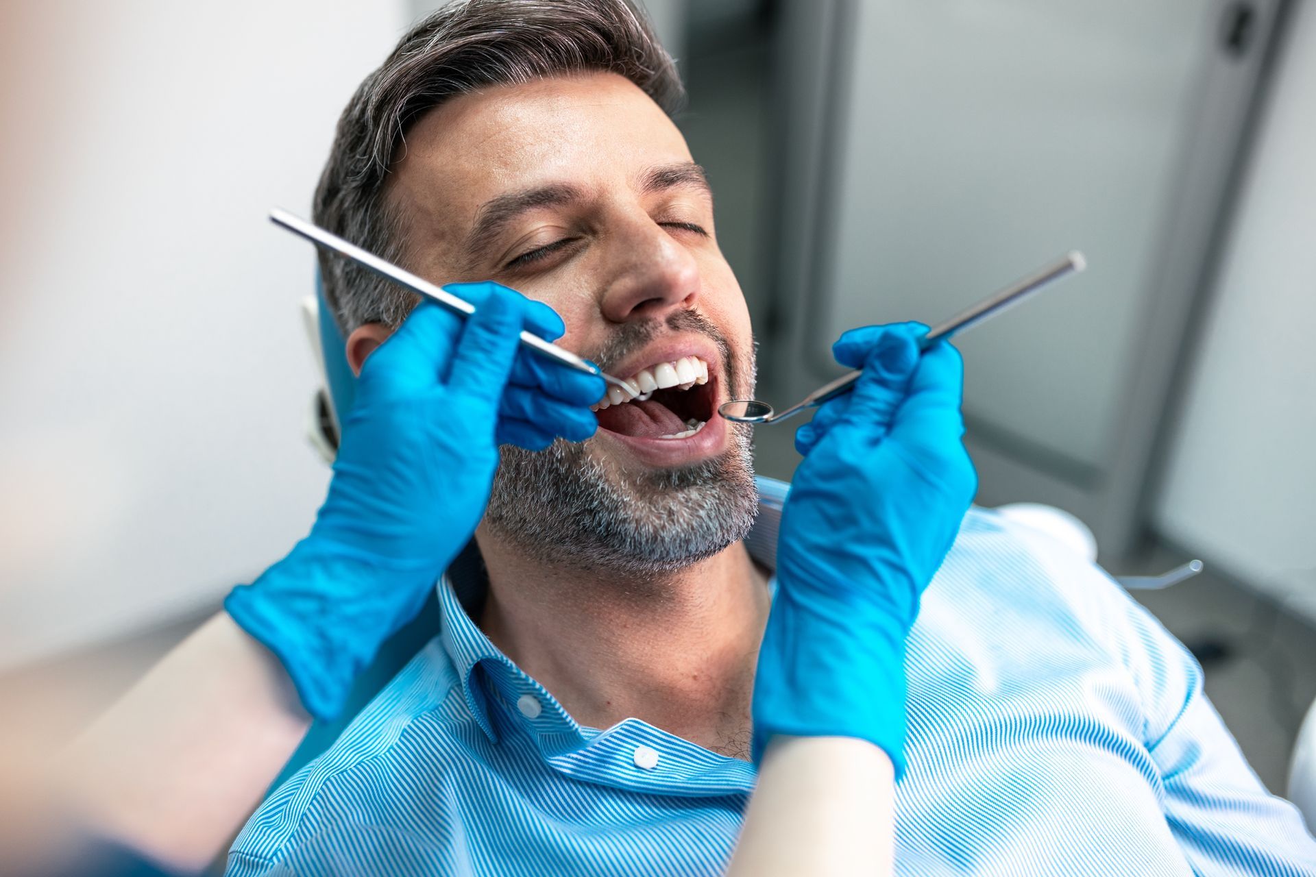 Patient getting restorative dental care with his mouth open and dentist's hands with blue gloves.