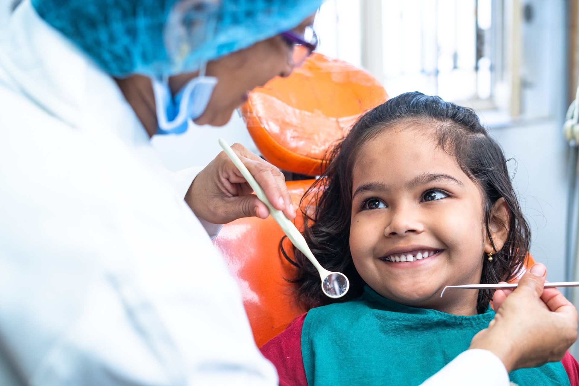 A smiling girl looking at a dentist while the dentist holds dental instruments.