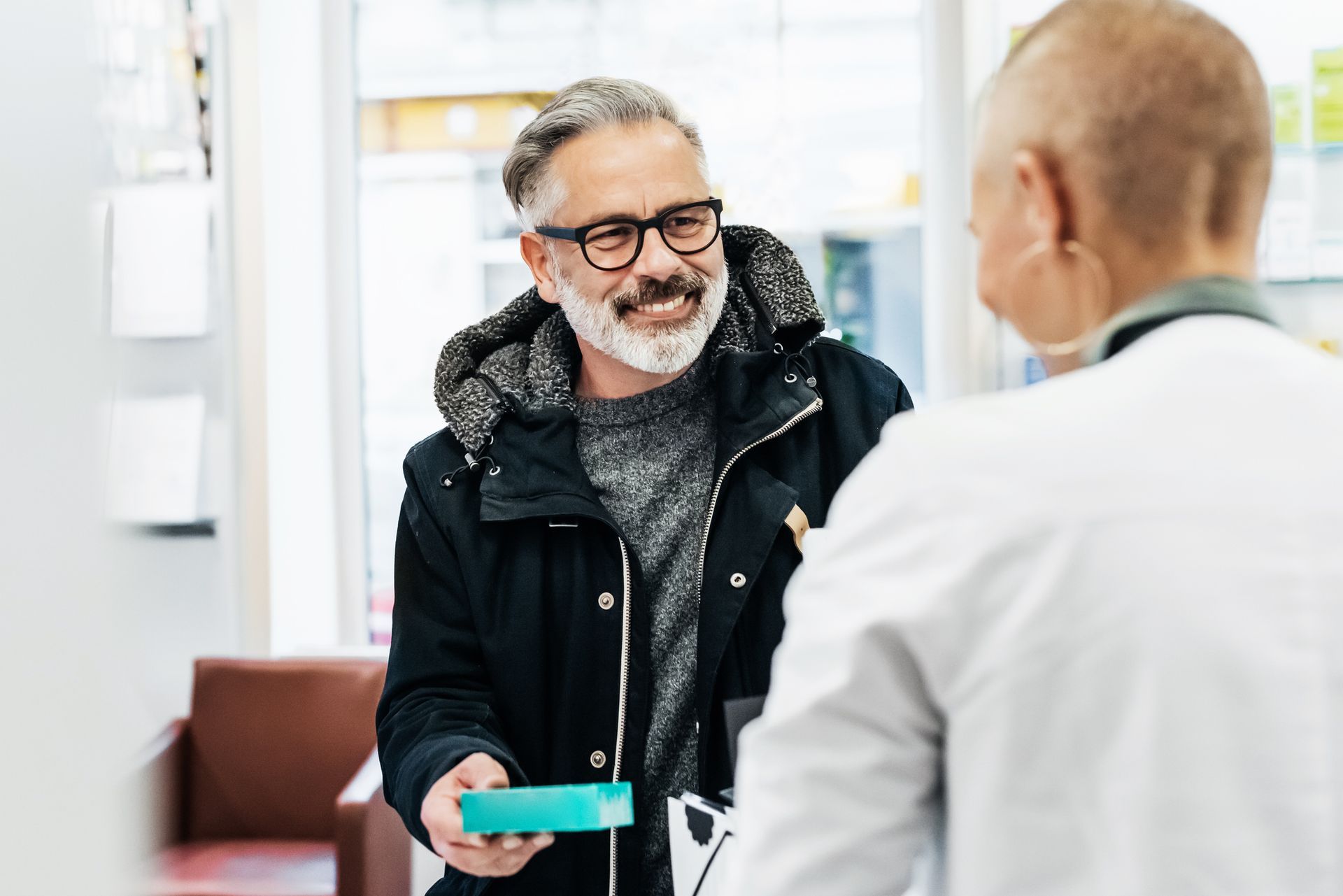 A man is giving a prescription to a pharmacist in a pharmacy.