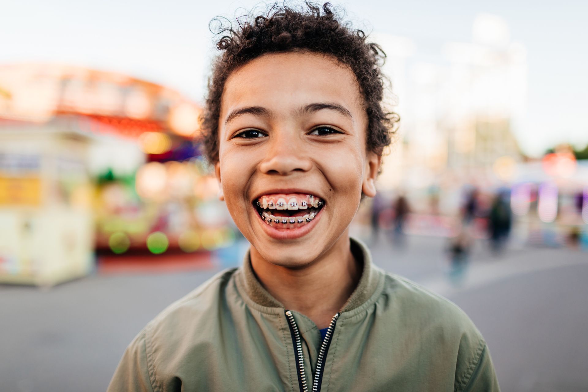 A young boy with braces is smiling at the camera at a carnival.