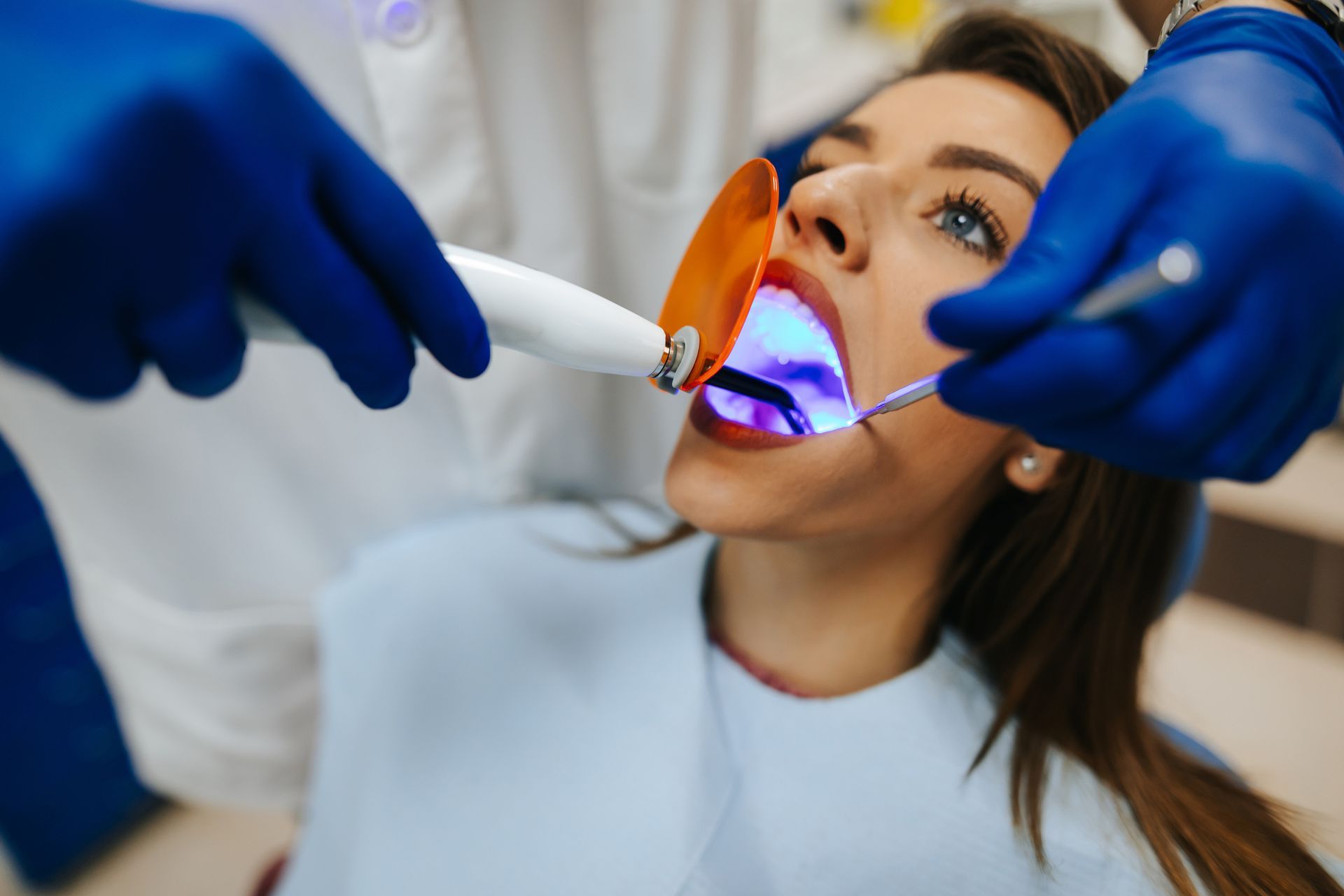 A woman with red lips is getting her teeth whitened by a dentist.