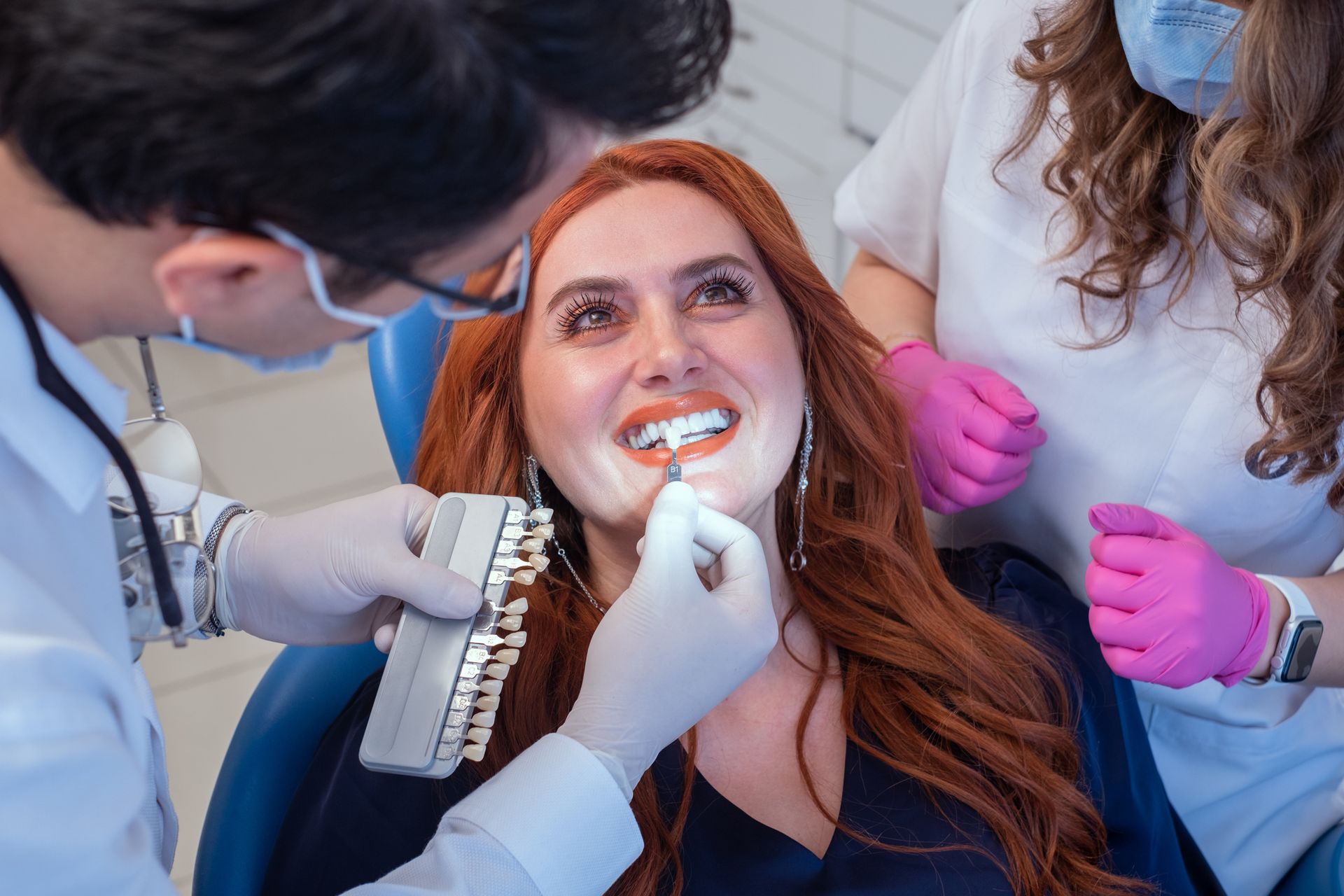 A woman with red hair is sitting in a dental chair while a dentist examines her teeth.
