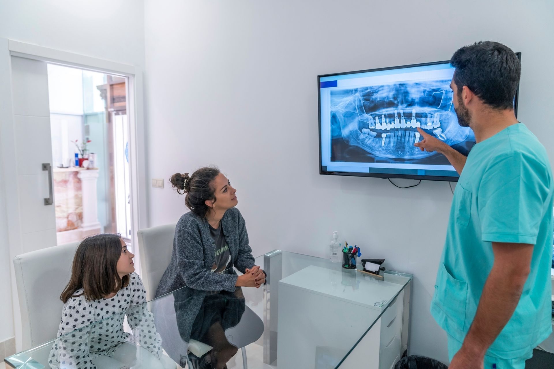 A dentist is talking to a woman and a child in a dental office.