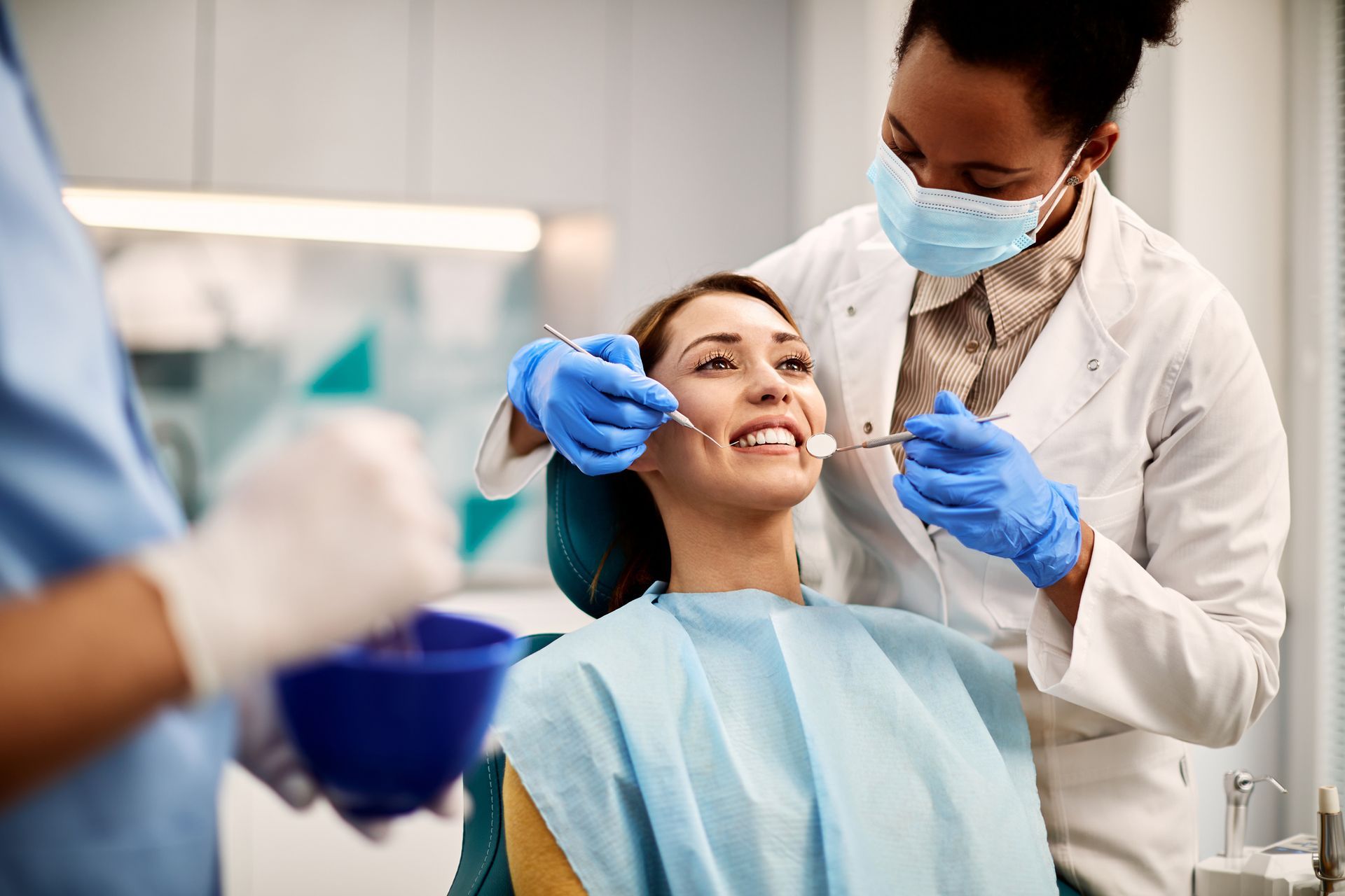 A happy woman is sitting in a dental chair while a dentist examines her teeth.