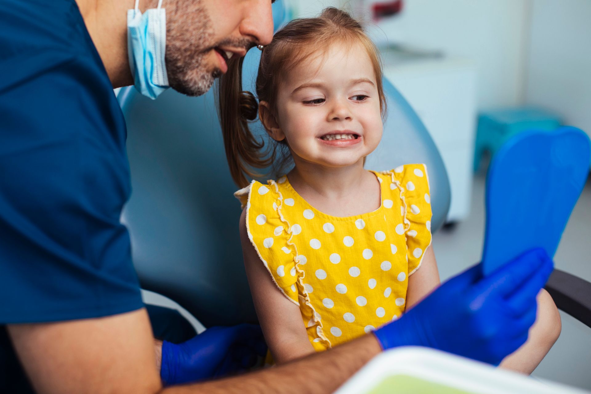 little girl looking at her smile in a blue mirror after having a routine checkup at the dentist.